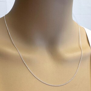 May include: A silver chain necklace on a mannequin. The chain is thin and delicate.