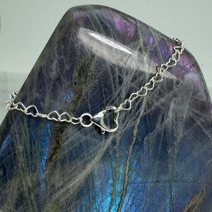 May include: A silver chain necklace with a heart-shaped clasp. The chain is made of small, delicate links.