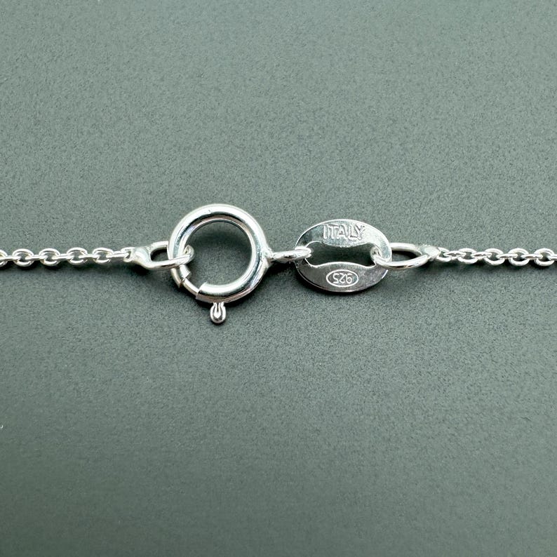 May include: Close-up of a silver chain necklace clasp with a lobster claw closure and a tag that reads "ITALY 925".