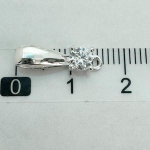 May include: A silver pendant with a clear round gemstone, measuring approximately 1 cm in diameter. The pendant has a bail for attaching to a chain.