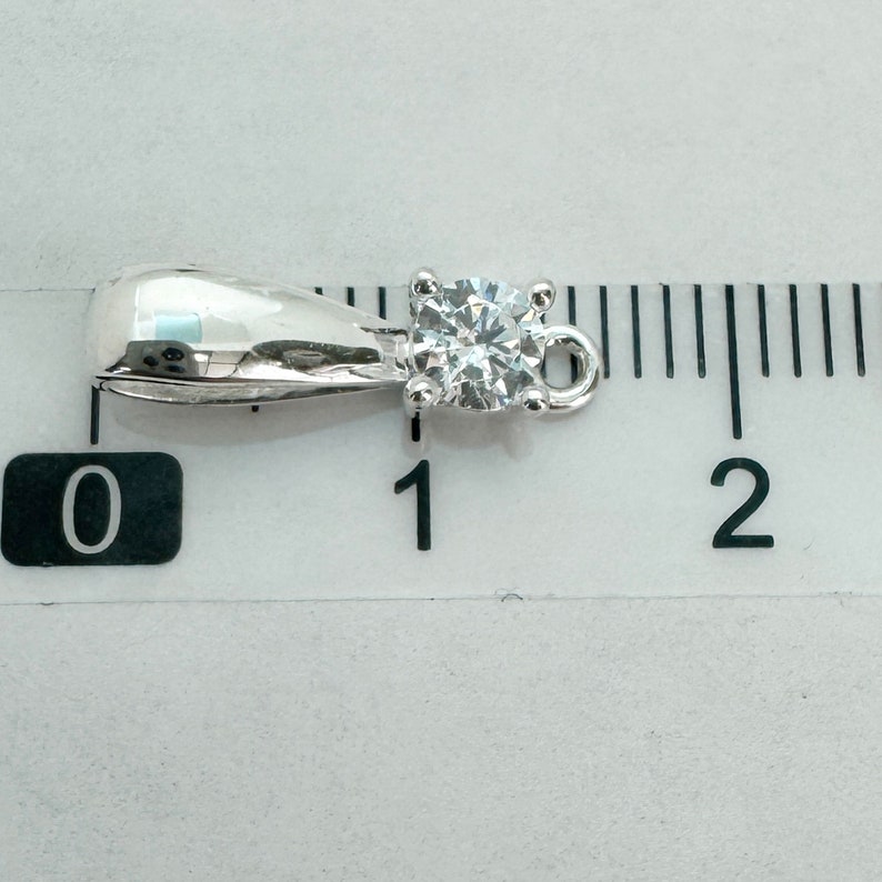 May include: A silver pendant with a clear round gemstone, measuring approximately 1 cm in diameter. The pendant has a bail for attaching to a chain.