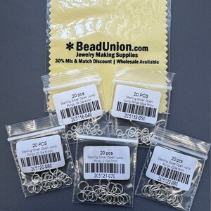 May include: Five small plastic bags containing 20 sterling silver open jump rings in various sizes. The bags are labeled with the size and gauge of the rings, as well as the product code. The bags are on a yellow polishing cloth with the text "BeadUnion.com Jewelry Making Supplies 30% Mix & Match Discount | Wholesale Available".