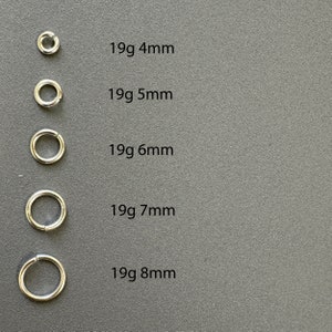 May include: Five silver jump rings of different sizes, from 4mm to 8mm in diameter. Each ring is labeled with its size in millimeters and gauge in grams.