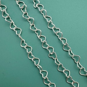 May include: Three silver chains with heart-shaped links. The chains are laid out on a green surface.