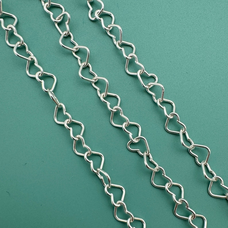 May include: Three silver chains with heart-shaped links. The chains are laid out on a green surface.