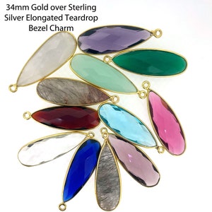 May include: A collection of 12 gold-plated teardrop-shaped gemstone charms. The charms are made of various materials, including clear quartz, amethyst, green aventurine, and rose quartz. Each charm has a gold bail for attaching to jewellery.