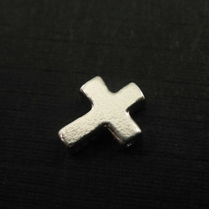 May include: A silver cross charm with a textured surface.