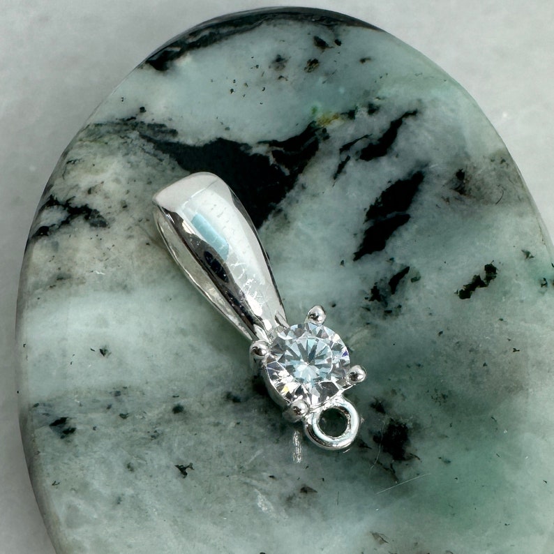 May include: Silver pendant with a clear round gemstone and a loop for attaching a chain.