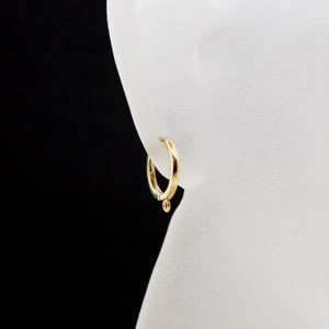 Op de afbeelding: Een paar gouden oorringen met een kleine bol aan de onderkant van de ring.