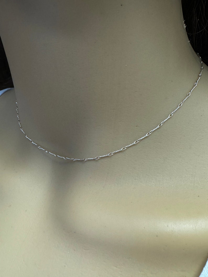 May include: A delicate silver chain necklace with a simple design. The chain is made of small, linked circles.