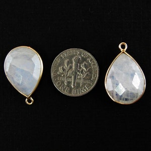 Two moonstone pendants are displayed with a dime between them to indicate size. the pendants are about the size of a dime.
