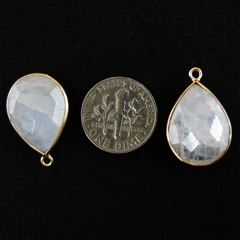 Two moonstone pendants are displayed with a dime between them to indicate size. the pendants are about the size of a dime.