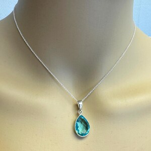 May include: A silver chain necklace with a teardrop-shaped pendant featuring a light blue gemstone.