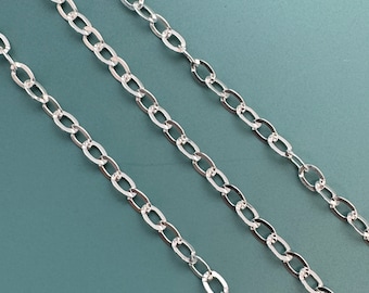 Puede incluir: Tres cadenas de plata con un diseño de eslabón ovalado plano. Las cadenas están dispuestas en líneas paralelas sobre un fondo azul.