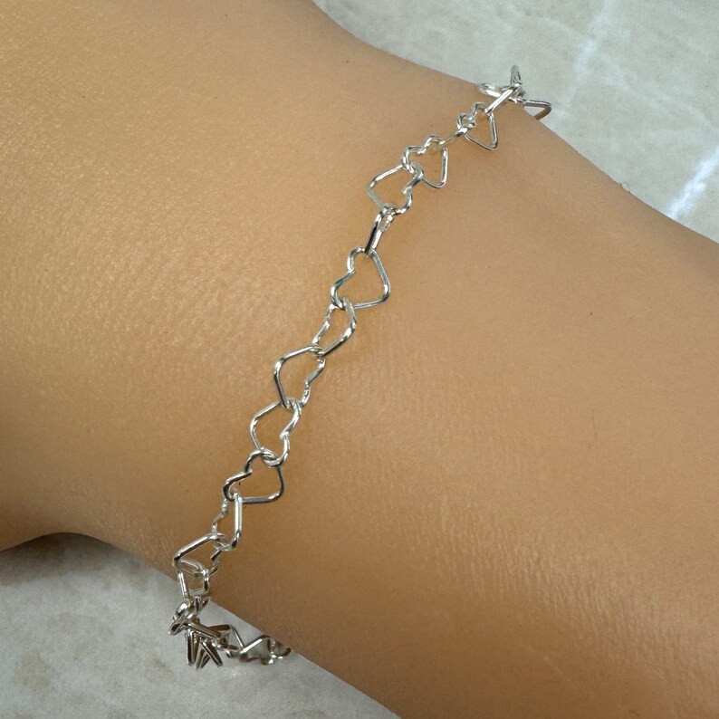 May include: A silver heart-shaped chain bracelet. The bracelet is made of small, interconnected heart-shaped links.