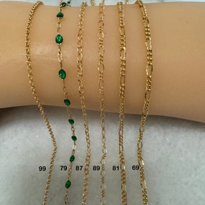 K&ouml;nnte beinhalten: Sechs goldene Ketten mit verschiedenen Gliederarten, darunter eine Kette mit gr&uuml;nen Edelsteinen. Die Ketten sind mit den Nummern 99, 79, 87, 89, 81 und 69 gekennzeichnet.