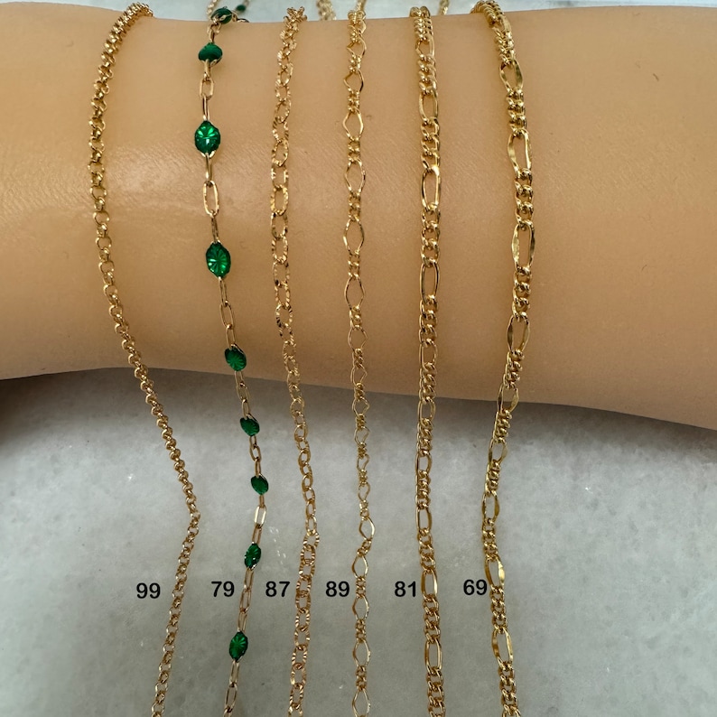 K&ouml;nnte beinhalten: Sechs goldene Ketten mit verschiedenen Gliederarten, darunter eine Kette mit gr&uuml;nen Edelsteinen. Die Ketten sind mit den Nummern 99, 79, 87, 89, 81 und 69 gekennzeichnet.