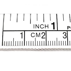 May include: A silver chain necklace measuring 1 inch (2.5 cm) in length, displayed on a ruler.