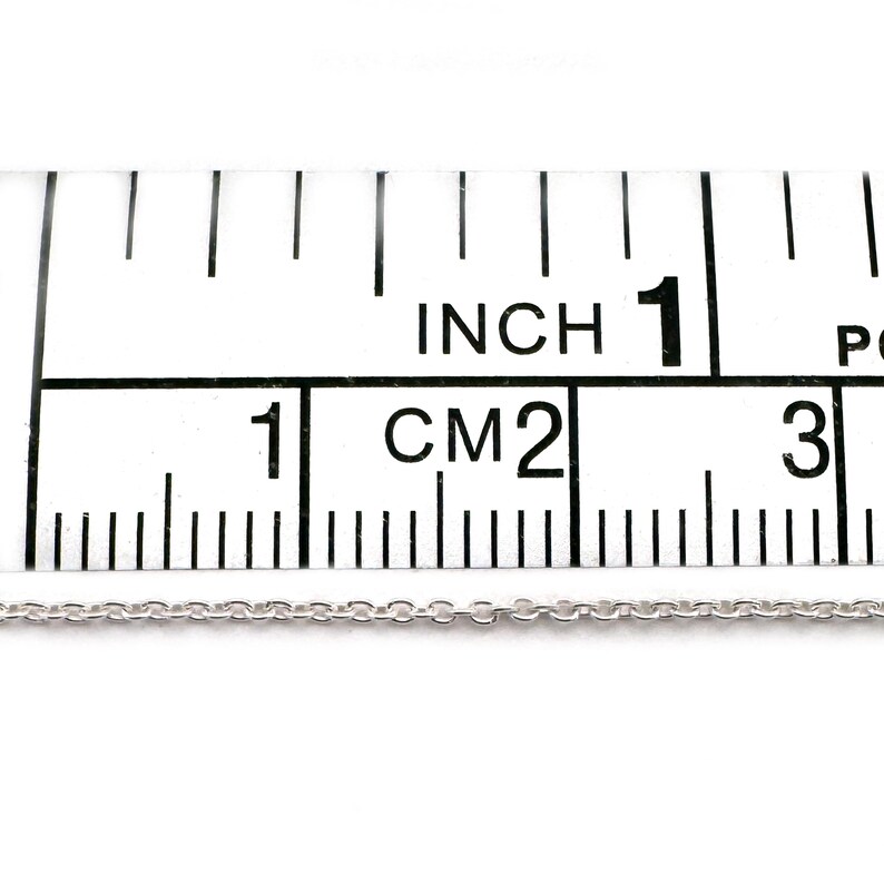 May include: A silver chain necklace measuring 1 inch (2.5 cm) in length, displayed on a ruler.