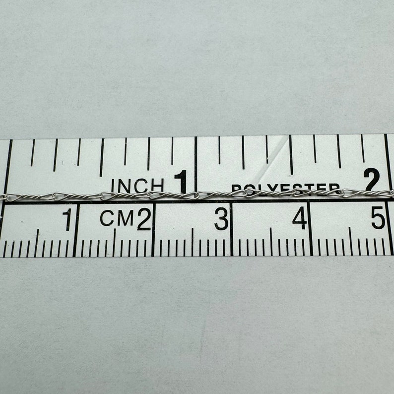 May include: A close-up of a silver chain measured against a ruler. The chain is approximately 1 inch (2.5 cm) long.