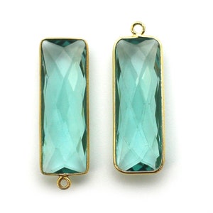 Puede incluir: Dos colgantes rectangulares de cristal azul turquesa con marcos de metal dorado y anillas de salto.