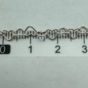 May include: Close-up of a silver heart-shaped chain measured on a ruler. The chain is approximately 2 inches long.