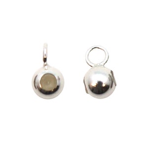 Puede incluir: Dos pequeños componentes de joyería plateados y brillantes. Cada componente es una semiesfera con un lazo en la parte superior para sujetarlo a otras joyas. Los componentes están diseñados para la fabricación de joyas.