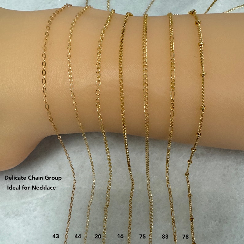 K&ouml;nnte beinhalten: Nahaufnahme von zehn goldenen Ketten in verschiedenen Stilen und L&auml;ngen. Die Ketten liegen auf dem Arm einer Person. Die Ketten sind mit Zahlen beschriftet: 43, 44, 20, 16, 75, 83, 78. Der Text "Delicate Chain Group Ideal for Necklace" ist am unteren Rand des Bildes sichtbar.