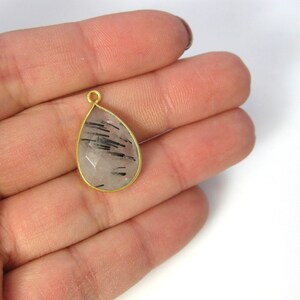 A gold rutilated quarts pendant is displayed on a hand to indicate size