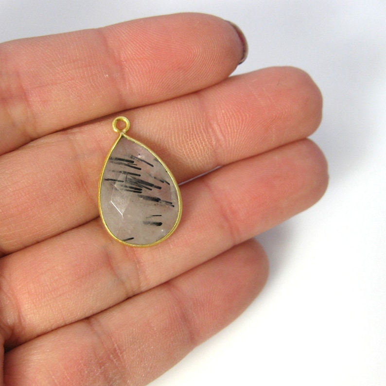 A gold rutilated quarts pendant is displayed on a hand to indicate size