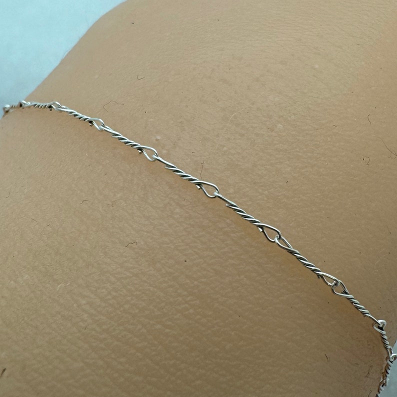 May include: A silver chain necklace with a twisted rope design and small oval links.
