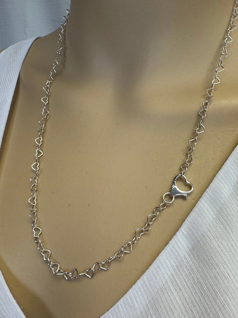 May include: A silver heart-shaped chain necklace with a lobster clasp closure.