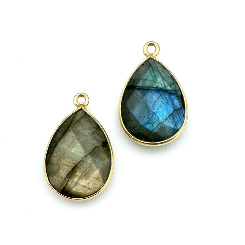 May include: Two teardrop-shaped labradorite gemstone pendants with gold-toned bezels and jump rings. The pendants are on a white background.