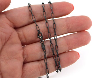 May include: A black chain necklace with a box chain design. The chain is lying on a hand.