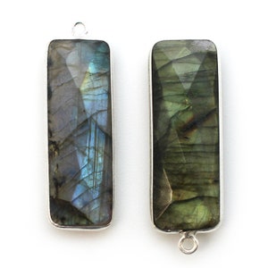 May include: Two silver-toned pendant charms with rectangular labradorite stones. The stones have a dark green and blue iridescent sheen.