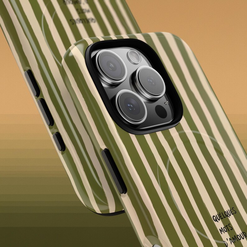 May include: A close-up of two phone cases. The cases have a green and beige striped pattern. The phone case in the foreground has a black camera housing. The text "QUELQUES MOTS D'AMOUR" is visible on the case.