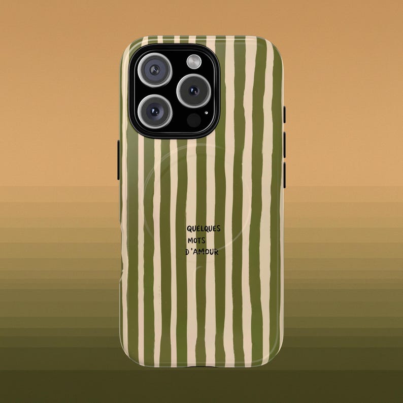 May include: A phone case with a vertical striped pattern in olive green and cream. The case has a camera module with three lenses and a flash. The text "QUELQUES MOTS D'AMOUR" is printed on the case.