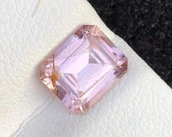 Peut inclure: Une pierre précieuse rose clair taillée à l'émeraude. La gemme est posée sur une surface blanche avec un fond sombre. Les facettes du joyau reflètent la lumière, créant un effet scintillant. La gemme est de forme carrée avec des coins coupés.