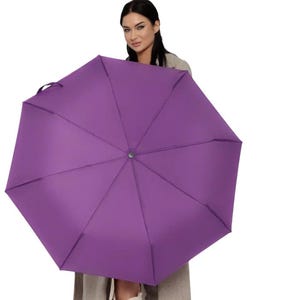 Peut inclure: Une femme tient un parapluie violet au-dessus de sa t&ecirc;te. Le parapluie est ouvert et la femme regarde la cam&eacute;ra.