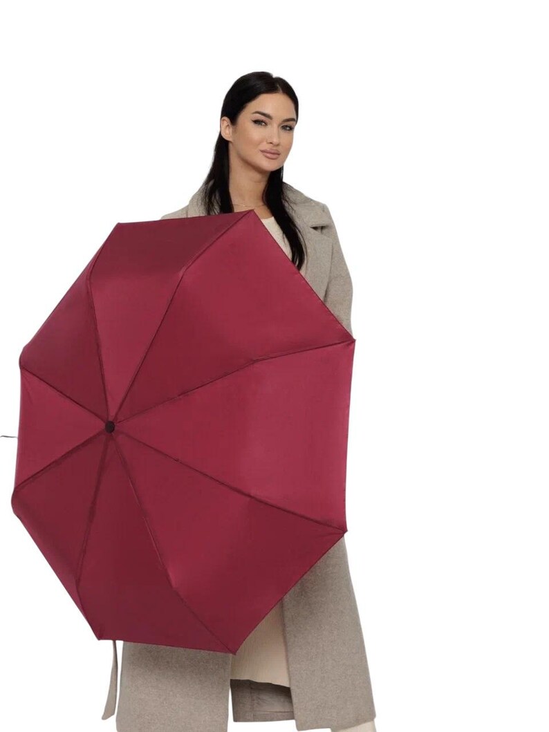 Peut inclure: Une femme tenant un parapluie bordeaux. Le parapluie est ferm&eacute; et a une poign&eacute;e noire.