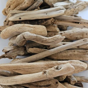 May include: A collection of weathered driftwood pieces in various shapes and sizes. The wood tones range from light beige to darker browns, with visible textures and natural holes. The pieces are arranged in a pile, suggesting a natural, rustic theme.