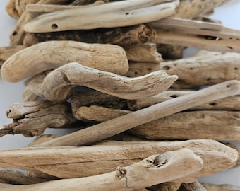 May include: A collection of weathered driftwood pieces in various shapes and sizes. The wood tones range from light beige to darker browns, with visible textures and natural holes. The pieces are arranged in a pile, suggesting a natural, rustic theme.