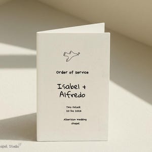 以下が含まれることがあります： 「Order of service」の文字と「Isabel + Alfredo」の名前が書かれたクリーム色のウェディングプログラム。日付「20 Dic 2026」と場所「Alberston wedding chapel」も印刷されています。上部には小さな鳩のイラストがあります。