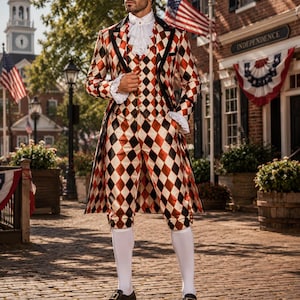Op de afbeelding: Een pandjesjas, gilet en kniebroek met een rood, wit en zwart ruitpatroon. De outfit bevat een witte kanten jabot, witte kanten mouwboorden, witte kniekousen en zwarte schoenen met gespen.