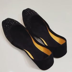 Puede incluir: Un par de bailarinas negras con textura de terciopelo. La zona de la puntera est&aacute; adornada con peque&ntilde;os pedrer&iacute;a de color oscuro. El forro interior es de color amarillo brillante.