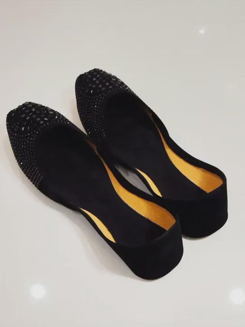 Puede incluir: Un par de bailarinas negras con textura de terciopelo. La zona de la puntera est&aacute; adornada con peque&ntilde;os pedrer&iacute;a de color oscuro. El forro interior es de color amarillo brillante.
