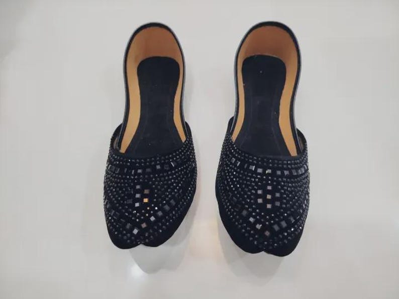 Puede incluir: Un par de zapatos negros sin cordones con un patr&oacute;n decorativo de peque&ntilde;os adornos cuadrados. Los zapatos tienen una punta redondeada y un interior de color beige.