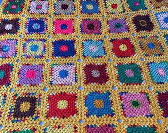 Könnte beinhalten: Eine bunte Häkeldecke mit gelbem Hintergrund und Quadraten in verschiedenen Farben, darunter Rot, Blau, Grün, Lila und Braun.