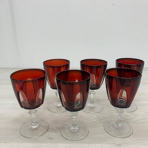 Puede incluir: Un juego de seis copas de vino con cuencos de cristal rojo intenso y paneles verticales tallados. Cada copa tiene un tallo transparente facetado y una base circular de cristal transparente. Los cuencos tienen una forma ancha y redondeada.
