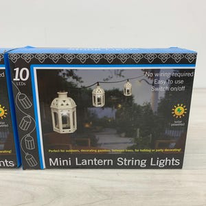 May include: A product box for mini lantern string lights featuring 10 LEDs. The packaging displays a graphic of white, cage-style lanterns on a string, labeled as solar powered with no wiring required and an on/off switch for outdoor use.